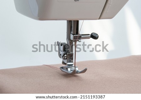 A sewing machine sews a light-colored fabric close-up. Detailed photo of the operation of the needle shuttle. Clothing industry, seamstress workplace, tailoring workshop concept