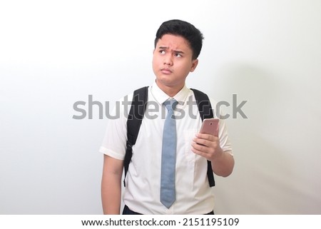 Indonesian senior high school student wearing white shirt uniform with gray tie showing confusion face expression while holding a mobile phone. Isolated image on white background