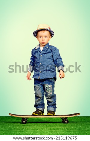 Portrait of a cute little boy in jeans clothes standing on a skateboard. Fashion. Childhood.