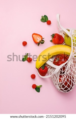Fruit in the crochet shopping bag on pastel pink background. Creative food concept. Tropical summer fruit idea. Healthy diet, vegetarian nutrition or grocery shopping banner. Flat lay.