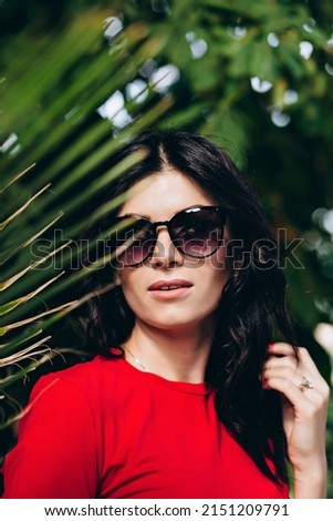 Fashion porter young brunette girl, close-up, in a red T-shirt on a background of palm trees