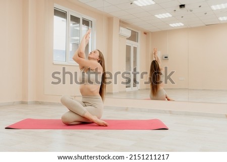 Young sporty woman, fitness instructor in sportswear doing stretching and pilates on yoga mat in the studio with mirror. Female fitness yoga routine concept. Healthy lifestyle and harmony.