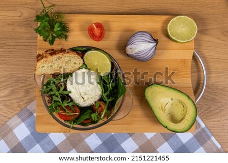 Homemade salad with italian cheese, burrata, eggs and vegetables and homemade bread on brown table and plaid and checked linen towel. 
