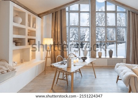 cozy warm home interior of a chic country chalet with a huge panoramic window overlooking the winter forest. open plan, wood decoration, warm colors and a family hearth Royalty-Free Stock Photo #2151224347