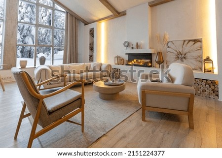 cozy warm home interior of a chic country chalet with a huge panoramic window overlooking the winter forest. open plan, wood decoration, warm colors and a family hearth Royalty-Free Stock Photo #2151224377