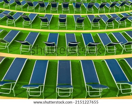 Lounge chairs on deck of luxury cruise ship. Rows of blue, empty chaise longue chairs create interesting patterns on green turf deck.