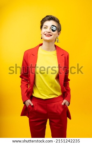 A young woman with a pirate patch over one eye. A sly expression on his face. Short haircut, red jacket, yellow T-shirt, bright yellow background in the studio, earrings. A modern pirate boss girl