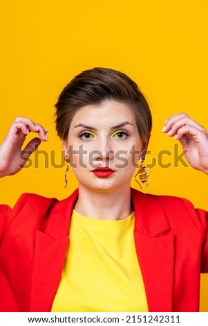 A large portrait of a business woman with short hair on a yellow background in a red jacket, correcting her hairstyle. Bright colors studio photo
