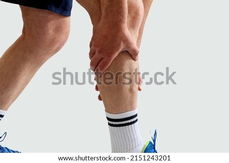 Man in sport clothes holding leg muscle pain and numbness from muscle cramps isolated on white background. Calf muscle pain in runner. 