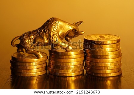 Metal bull with coins on a gold background. A symbol of financial success and independence.