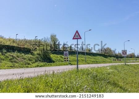 Country road with traffic signs: triangular warning caution with cyclists and maximum speed zone 60, green grass and trees in the background, sunny day with a blue sky in Netherlands