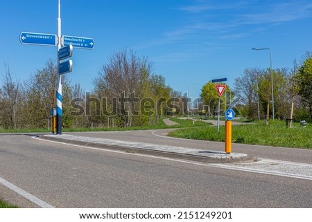 Rural road intersection, signs indicating the direction to Stevensweert, Maasbracht and Eindhoven, traffic signs: arrow indicating the direction to drive and give way in South Limburg, the Netherlands