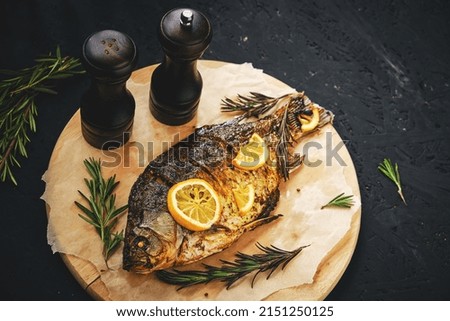 Baked fish in oven with lemon and rosemary laid out cutting board and parchment paper.On dark background with two straws