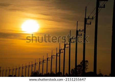 Row High Voltage Power Transmission Pylon lines Against red sunset Sky.