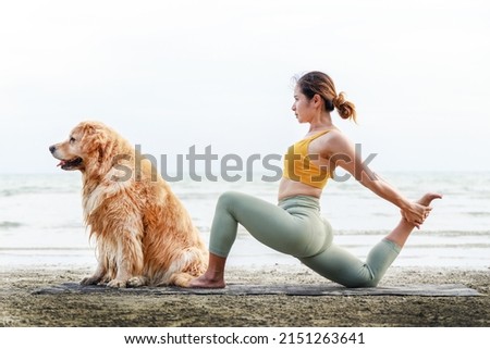 Banner size photo, an Asian young woman kisses her dog on a yoga mat on the beach. Relaxation with a pet.