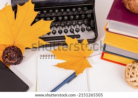 Autumn mood  On table are old typewriter, modern mobile phone, books, notebook and pen, dry yellow maple leaves  Workplace of student or writer 