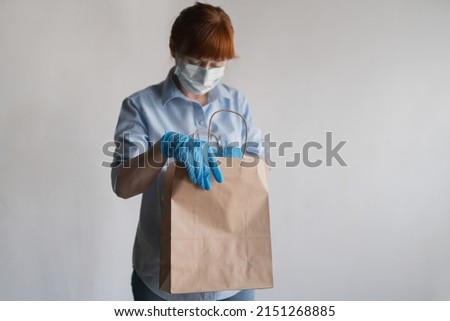 The girl in the means of individual protection sadly looks into an empty paper bag. Lack of food, hunger. High quality photo