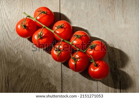 This is flat lay view of branch of cherry tomatoes on the wooden table. This is dark food photography of tomato,