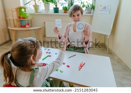 Female psychologist showing cards with positive and negative emotions faces to little girl Royalty-Free Stock Photo #2151283045