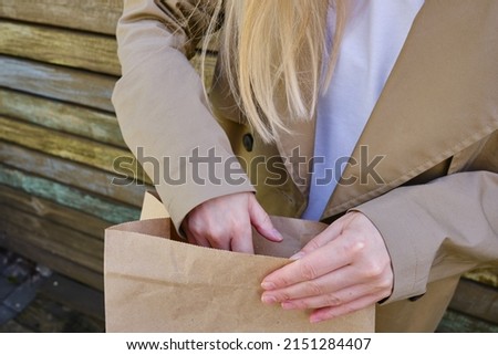 Craft paper bag in the hands of a girl. Gift wrapping. Food delivery service. Paper bag close up. Cardboard case. Blank space mockup for design, lettering or advertising