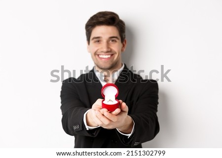 Image of handsome man looking romantic, giving you an engagement ring, making proposal to marry him, standing against white background