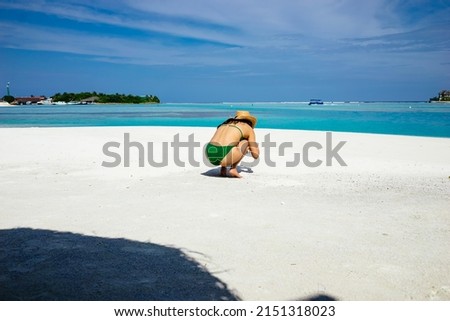 A woman in bikini focused on something on the white sand beach