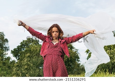The image of a young girl with a large piece of white material on the background of a rural evening landscape