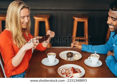 Caucasian woman taking a picture with her cellphone of a cheesecake while drinking coffee with her boyfriend