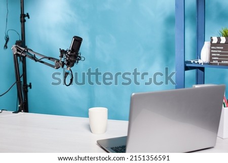 Professional microphone swivel boom arm stand in empty vlog broadcasting studio used for recording social media content. Audio live broadcast desk setup with digital mic and laptop computer.