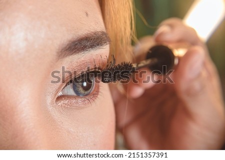 A makeup artist adds mascara to a client's eyelashes with a lash roller. Closeup view.