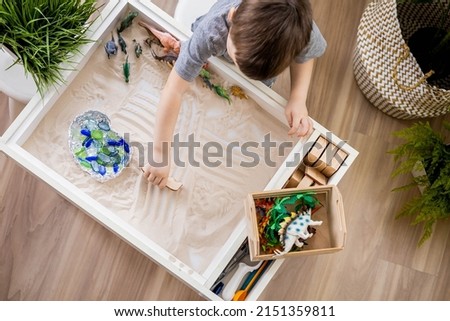 Focused baby boy confidently playing early development game kinetic sand Montessori material at cozy home. Adorable male child plays with carnivorous and herbivorous dinosaurs fine motor skills Royalty-Free Stock Photo #2151359811