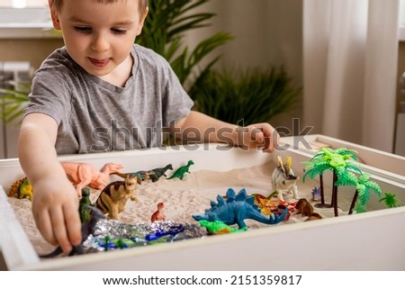 Cute baby boy playing sensory box dinosaur world kinetic sand table with carnivorous and herbivorous dinosaurs. Male kid enjoying early development game fine motor skills with Montessori material Royalty-Free Stock Photo #2151359817