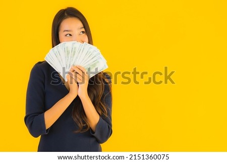 Portrait beautiful young asian woman with money and cash on yellow isolated background