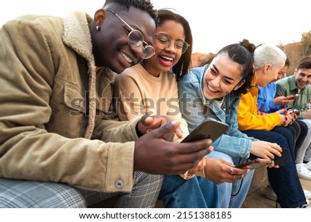 Happy multiracial teen college students having fun using mobile phone together in campus outdoors. Royalty-Free Stock Photo #2151388185