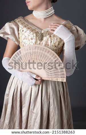 A Victorian woman wearing a gold ball gown and standing against a studio backdrop Royalty-Free Stock Photo #2151388263