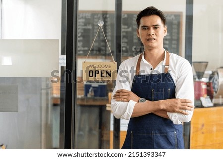 The coffee shop owner, a young Asian man in an apron, stands in front of the door with an open sign.
