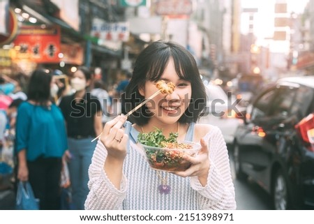Poeple travel and eating street food concept. Happy young adult asian foodie woman holding spicy grilled squid at southeast asia Chinatown market. Royalty-Free Stock Photo #2151398971