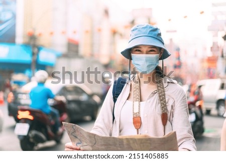 Attractive young adult traveller asian woman wear face mask for protect virus covid 19. Using map for sightseeing travel way trip and transport in the local city. Eye looking at camera