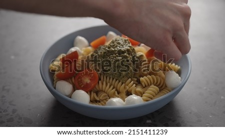 man add cherry tomatoes to pesto fusilli pasta in blue bowl on concrete background wide photo