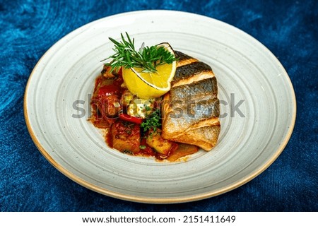 Grilled fish fillet plated with vegetables and lemon on blue background