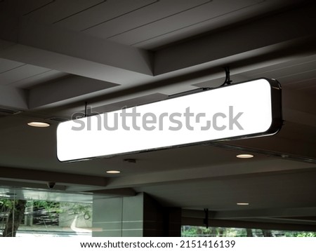 Hanging lightbox with blank space. Empty signage light box for advertising or directional sign, indoor. Sign board with black frame hanging on the ceiling, white strong structure in the dark building.