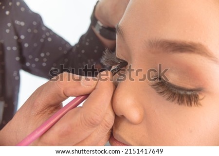 MUA adding thick eyeliner above the false eyelashes. Professional makeup techniques.