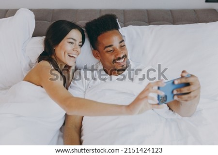 Top view smiling young couple two family man woman in casual white clothes lying in bed doing selfie shot on mobile cell phone rest relax spend time together in bedroom lounge room wake up good day