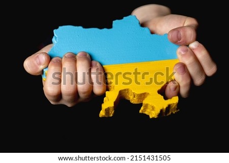 a map of Ukraine carved from wood and painted in the colors of the Ukrainian flag in the hands of a girl on a dark background