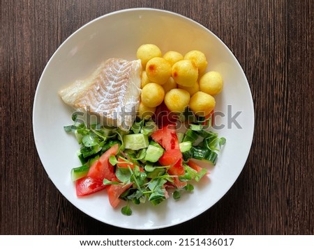 large vertical photo. homemade food. fried cod fillet with potato balls and fresh tomato and cucumber salad. young shoots of radishes. on a white round plate. top view close-up. useful and healthy foo