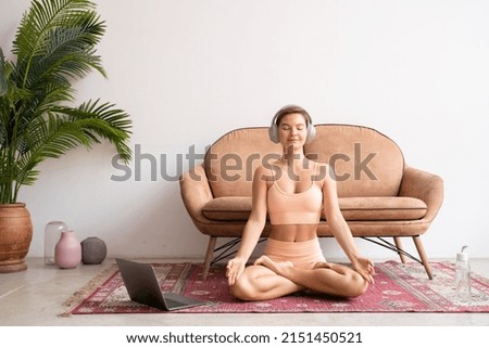 Young woman listening calm music for yoga meditation, sitting in lotus pose at home