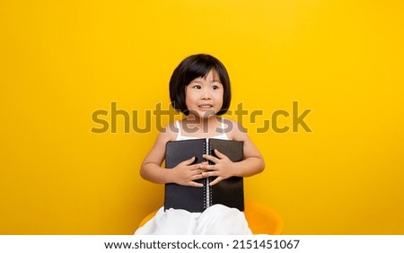 Close-up of a beautiful Asian woman reading a book on a yellow background in a photo studio.