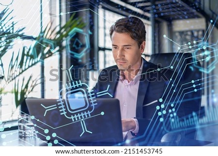 Handsome businessman in suit at workplace working with laptop to optimize development by implying new technologies in business process. Hi tech hologram over office background