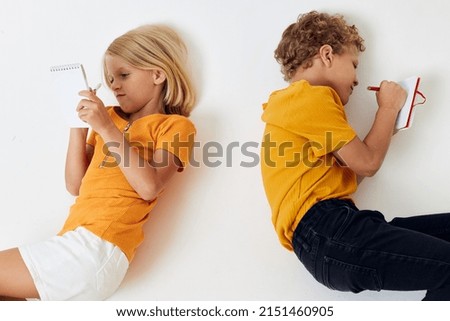 picture of positive boy and girl lie on the floor with notepads and pencils isolated background unaltered