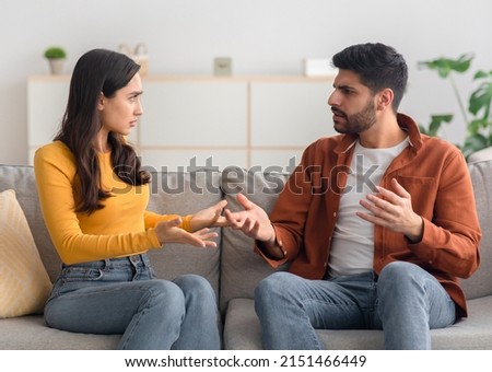 Angry Arabic Spouses Having Quarrel Arguing Looking At Each Other Sitting On Couch At Home. Domestic Violence And Abuse. Couple Struggling From Marital Crisis Concept Royalty-Free Stock Photo #2151466449